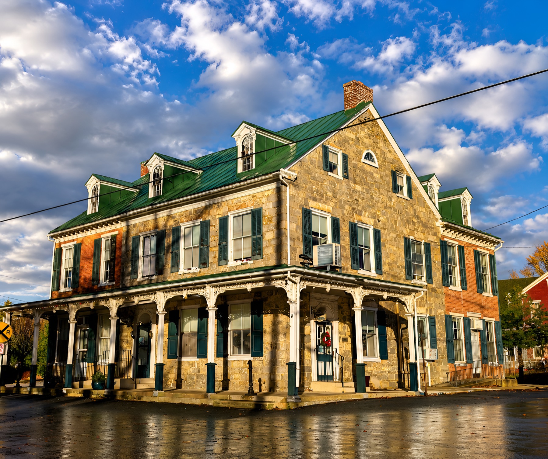The historic stone exterior of Bowers Hotel at golden hour — a three-story 1820s building with a green metal roof, dormer windows, and a wraparound porch